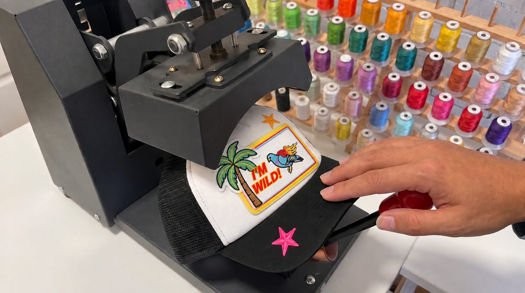 Mains posant un patch sur une casquette sous la presse, atelier Capaja